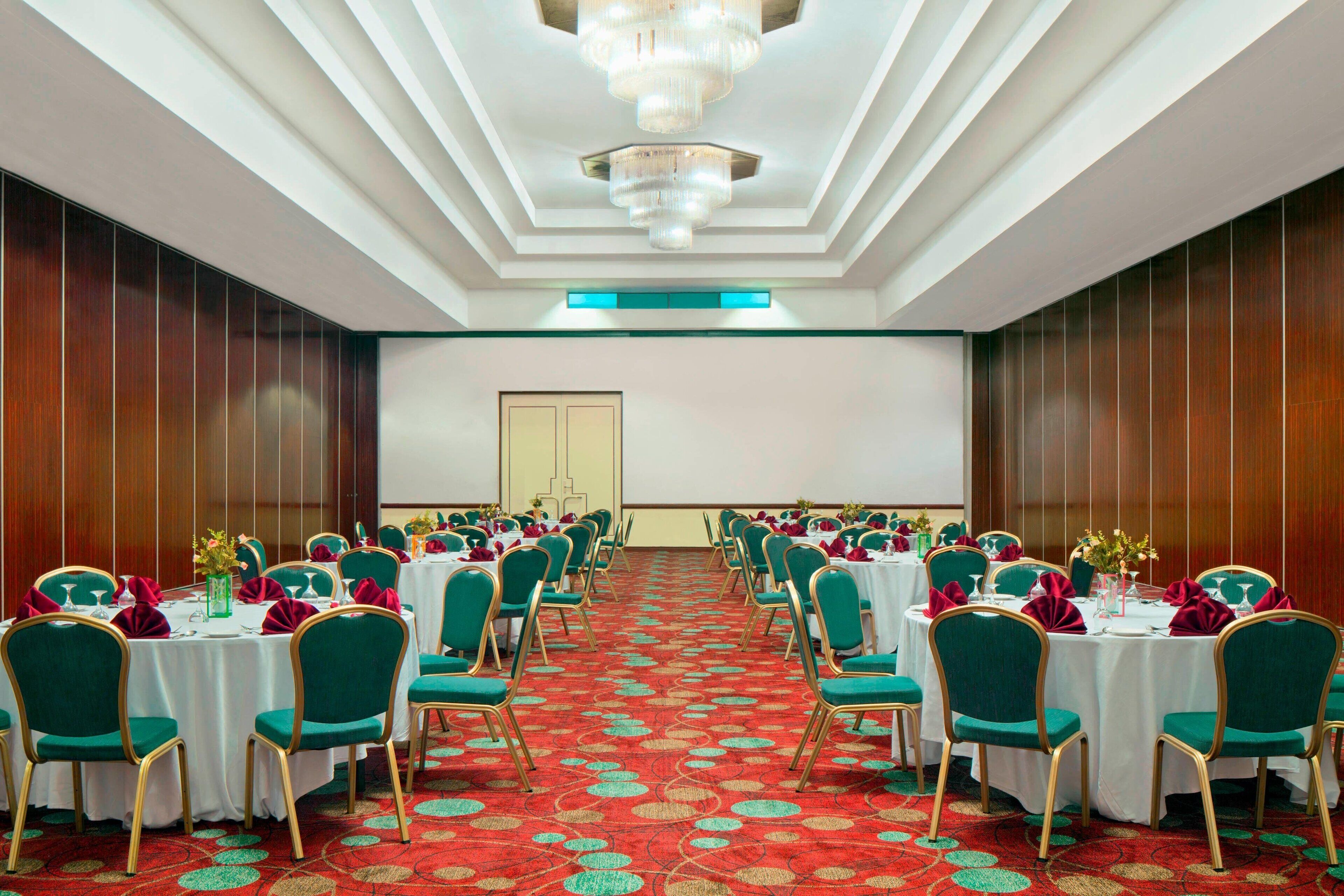 A conference room with rows of tables and chairs, a large screen, and a red carpeted floor.