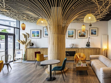 Un intérieur moderne avec une grande colonne en bambou, des tables rondes et un canapé.. Hôtel ibis Brest Centre