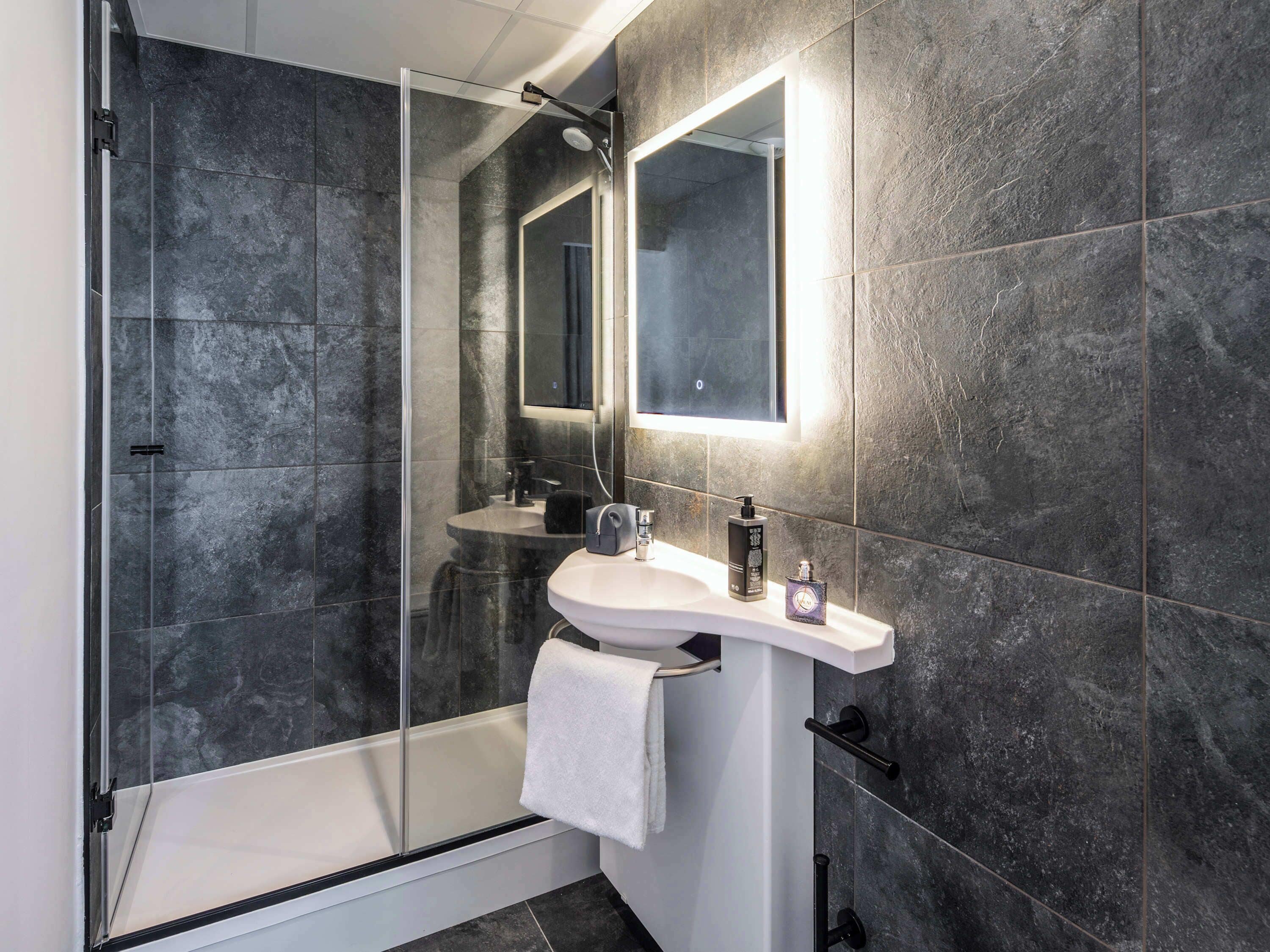 A modern bathroom with a glass shower enclosure, a white sink, and a mirror above it.