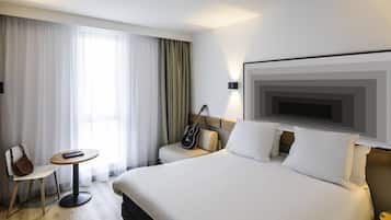 A hotel room with a large bed, a chair, a small table, and a guitar.