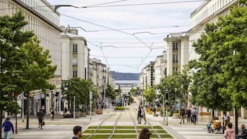 Une ligne de tramway avec des câbles aériens, un passage piétonnier et des bâtiments de part et d’autre.
