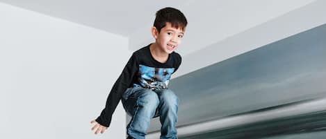 A child jumping on a bunk bed in a room with white walls and a simple, modern design.