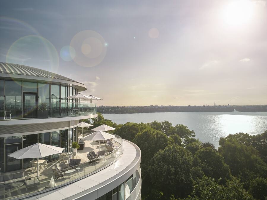 A modern building with a glass facade, outdoor seating, and a view of a body of water.