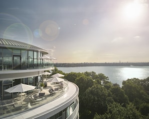 Un bâtiment moderne avec une façade en verre, des places assises en plein air et une vue sur un plan d’eau.