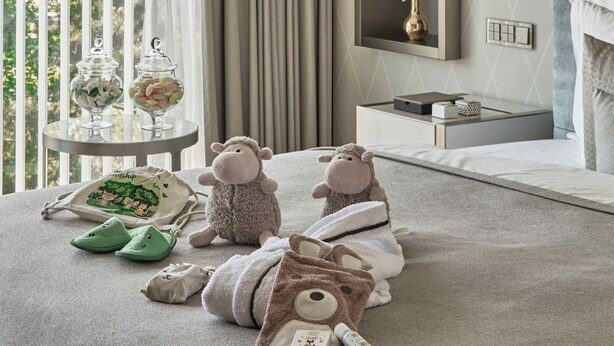 A bedroom with a large window, a bedside table with a lamp, and plush toys on the bed. - The Fontenay (Hamburg)