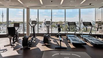 Un gimnasio con cintas de correr, elípticas y bancos de pesas, con amplias ventanas y vista a la ciudad.