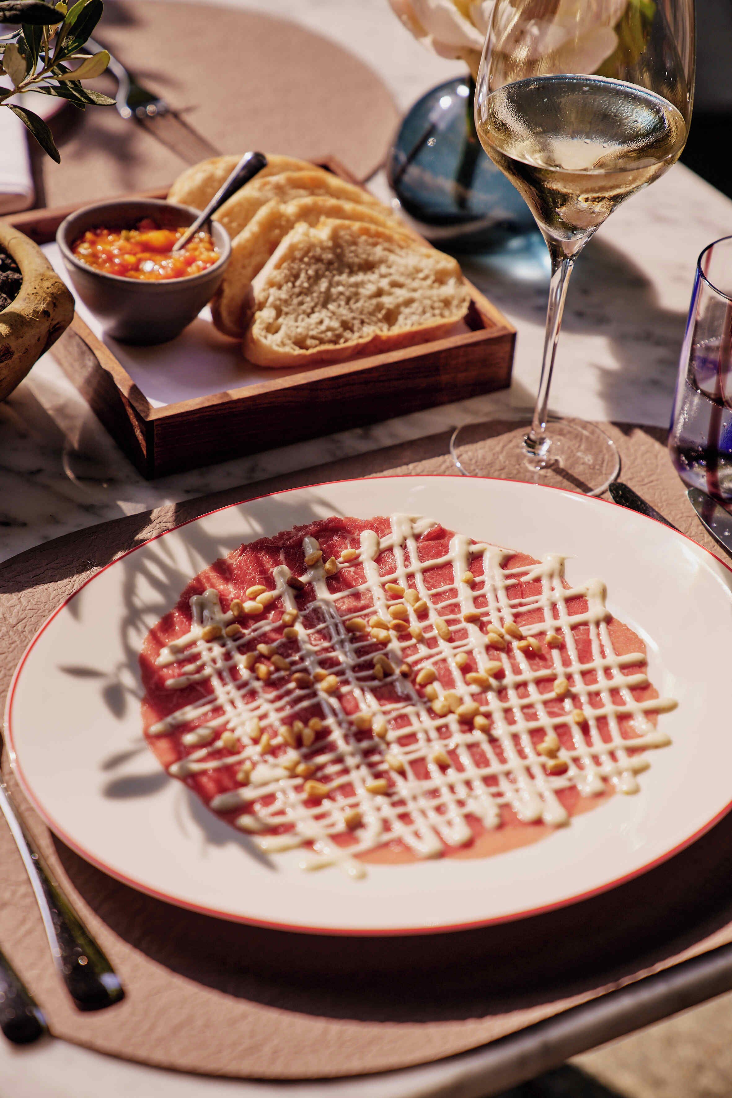 A dining table with a plate of food, a glass of white wine, and a bowl of sauce.