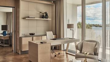 Una habitación de hotel moderna con un escritorio grande, un sillón cómodo y vistas a una masa de agua a través de ventanas amplias.