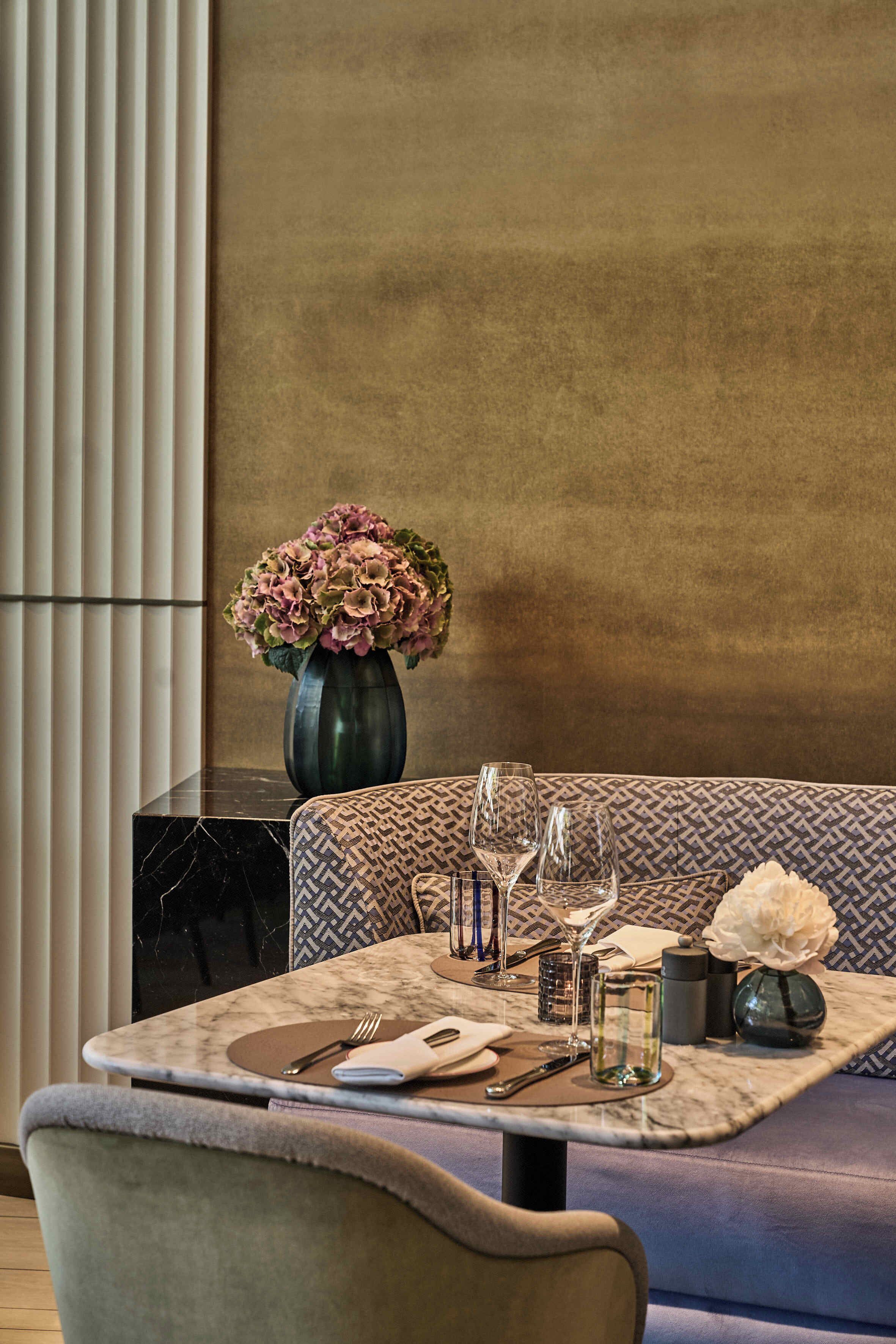 A dining area with a marble table, patterned cushions, and a vase of flowers.