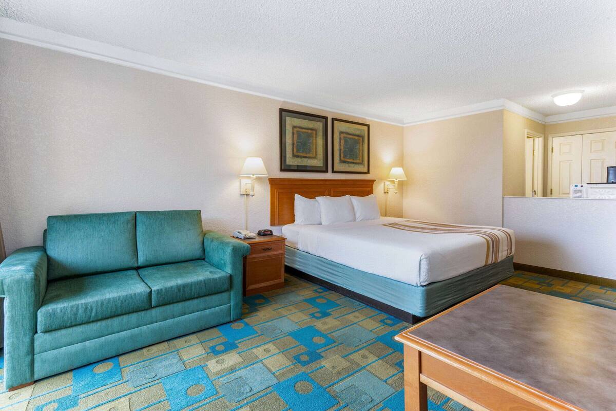 A hotel room with a bed, a sofa, a nightstand, two wall-mounted lamps, and a small table.