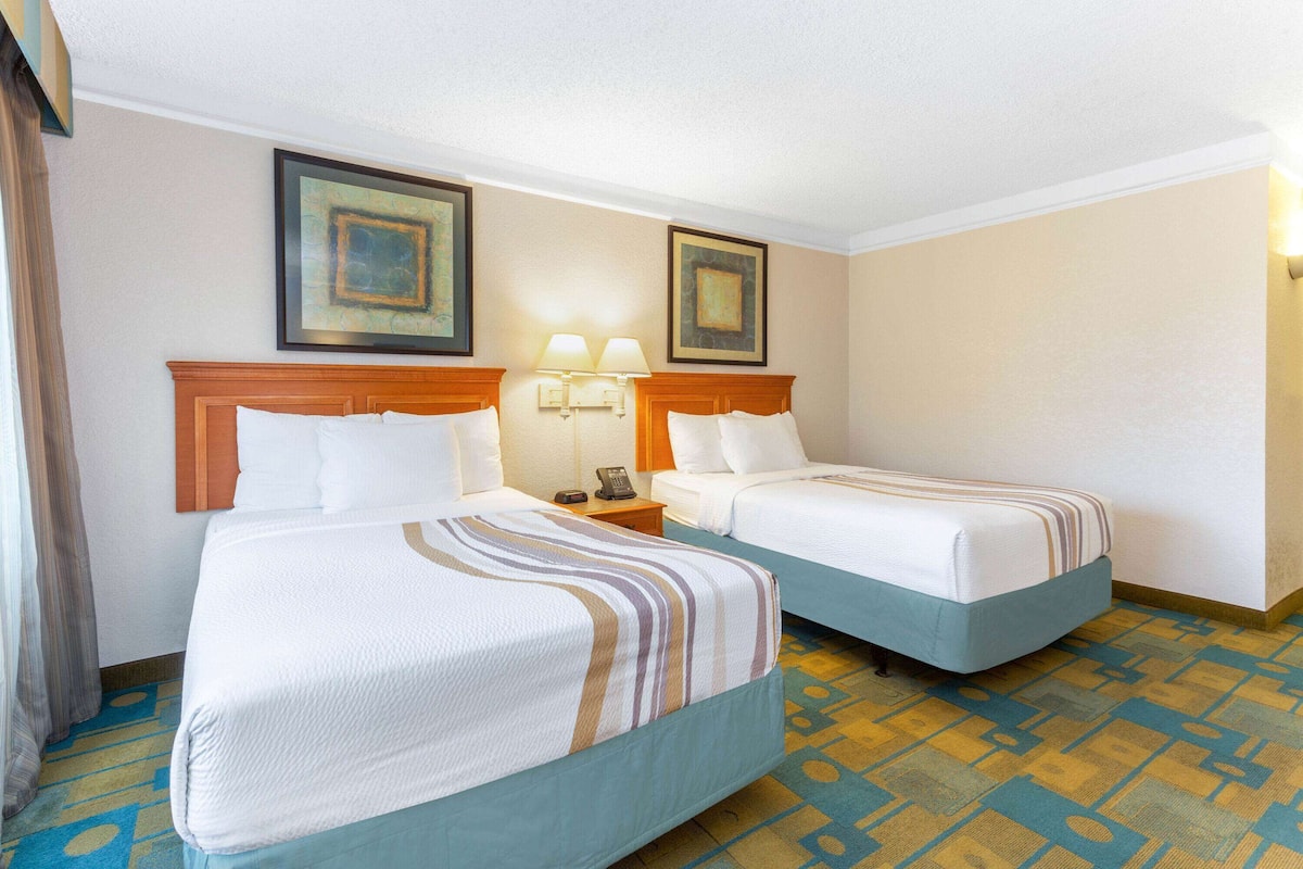 A hotel room with two beds, a nightstand with a lamp, and framed artwork on the wall.