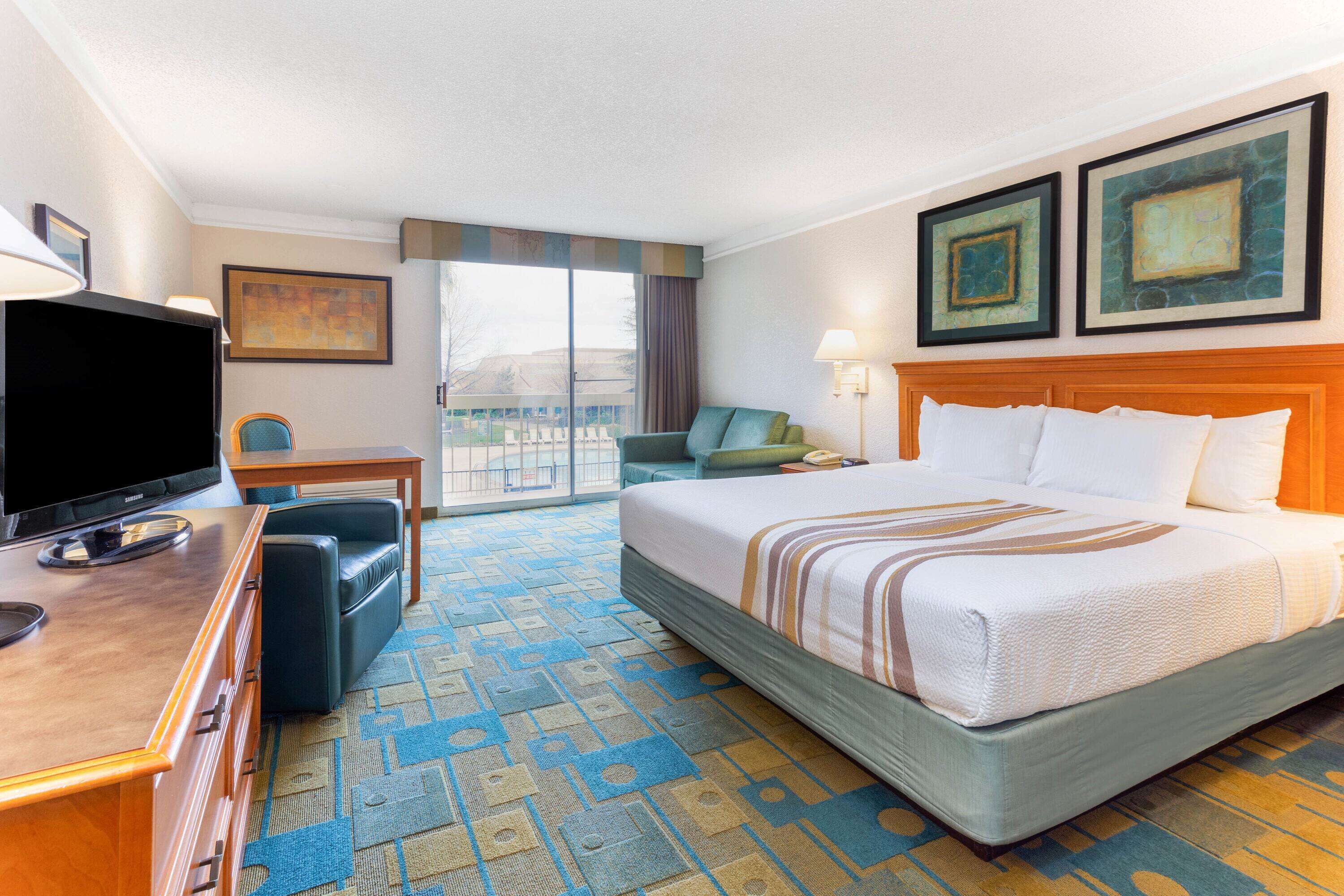 A hotel room with a bed, a television, a desk, a chair, and a view of the outside.