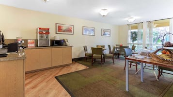 A hotel lobby with a reception desk, a popcorn machine, framed pictures on the wall, and a dining area with chairs and a table.