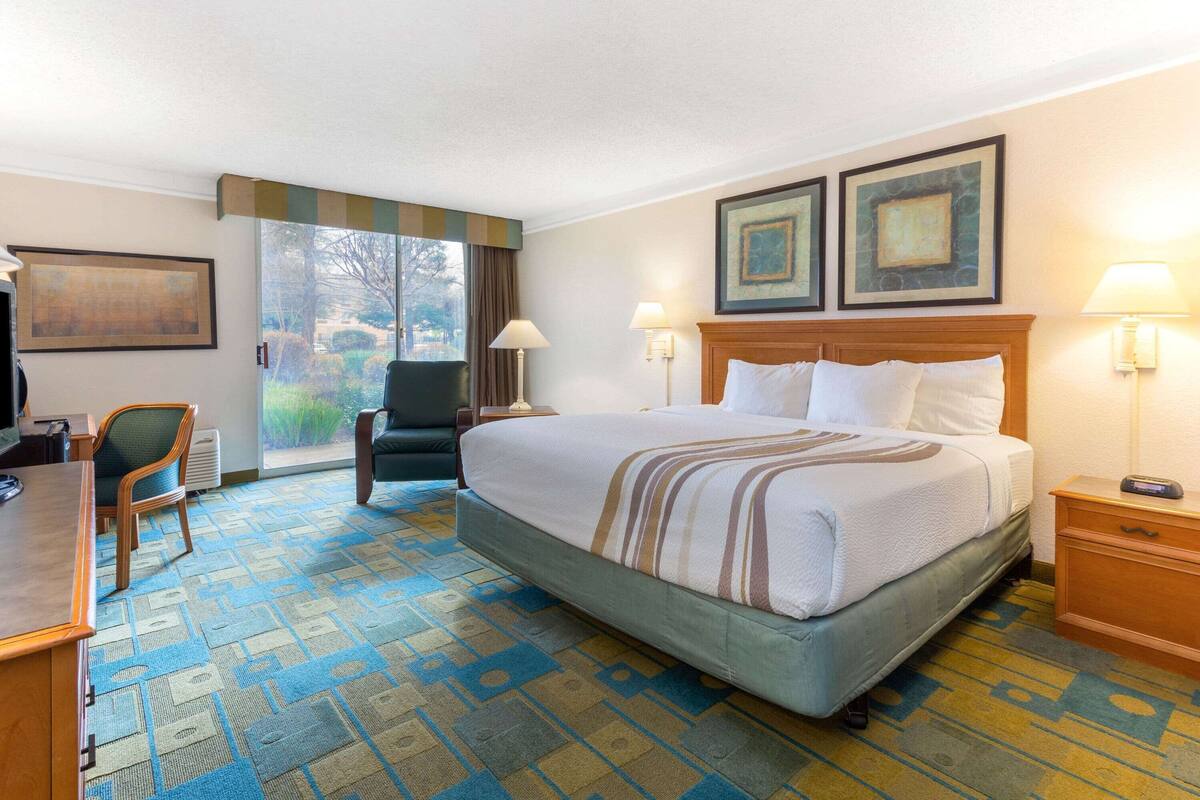 A hotel room with a large bed, a desk, a chair, and a view of the outdoors.