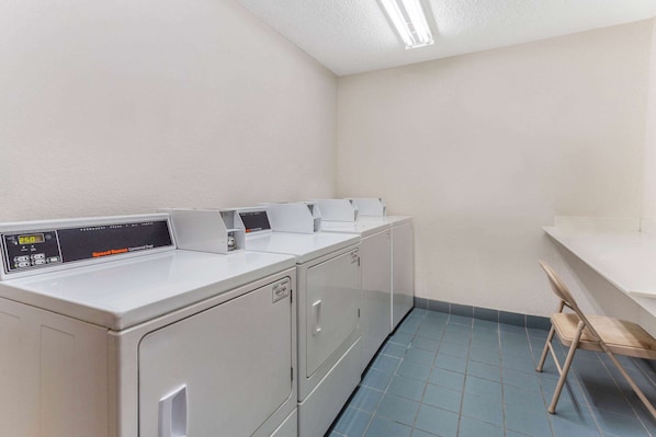 A laundry area with four white washing machines, a wooden chair, and a white countertop.