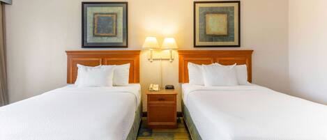 Habitación de hotel con dos camas, una mesita de noche con lámparas y obras de arte en las paredes.