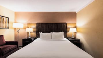 A hotel room with a large bed, two bedside tables with lamps, a dark headboard, and a single chair.