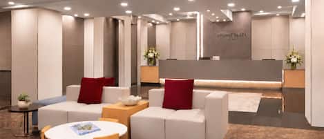 A modern lobby with seating areas, a reception desk, and a wall with signage.