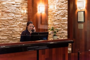 A reception desk with a stone wall backdrop, a framed certificate, and a potted plant. - Crowne Plaza Newark Airport by IHG (Elizabeth)