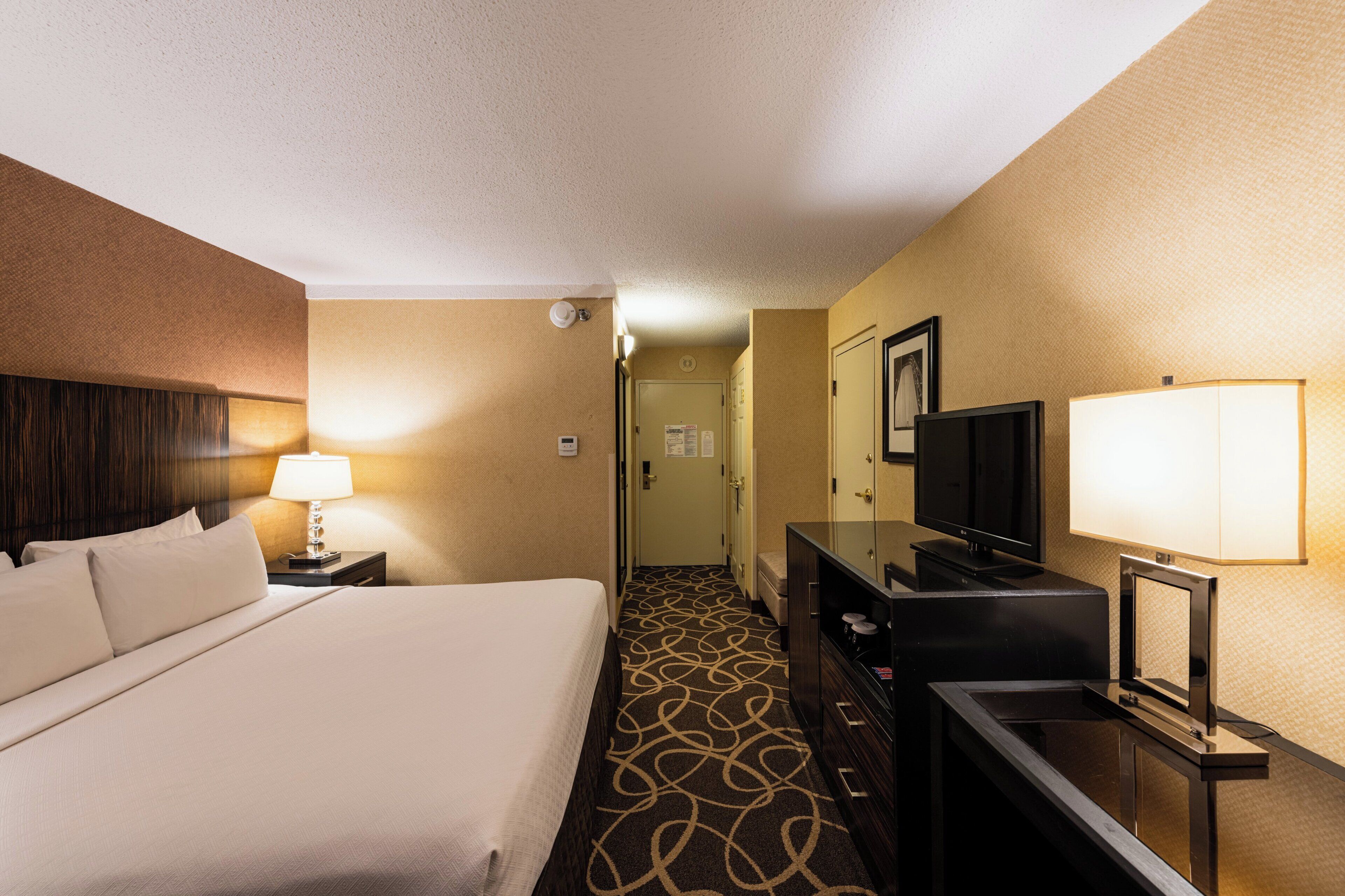 A hotel room with a bed, a desk, a television, and a lamp.