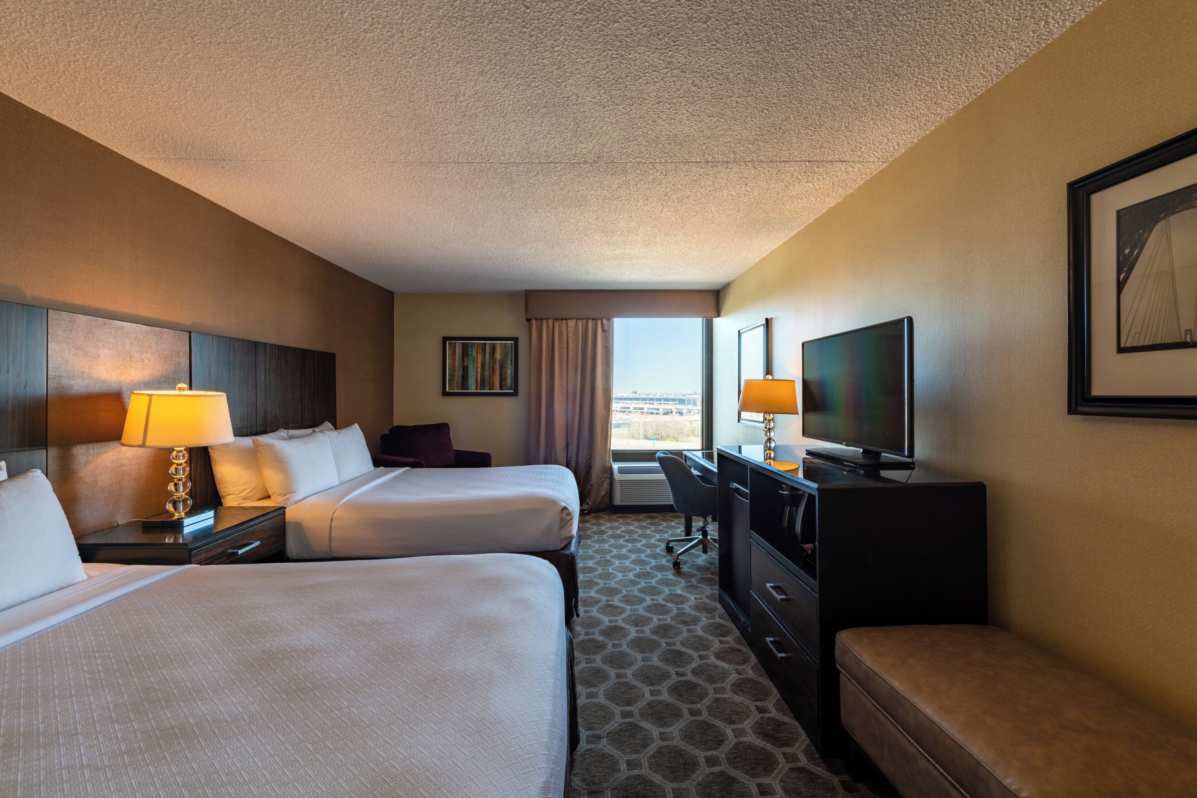 A hotel room with two beds, a desk, a television, and a window with a view.