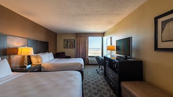 A hotel room with two beds, a desk, a television, and a window with a view.