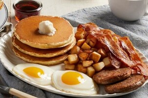 Un plato con tortitas, tocino, salchichas, huevos y patatas.