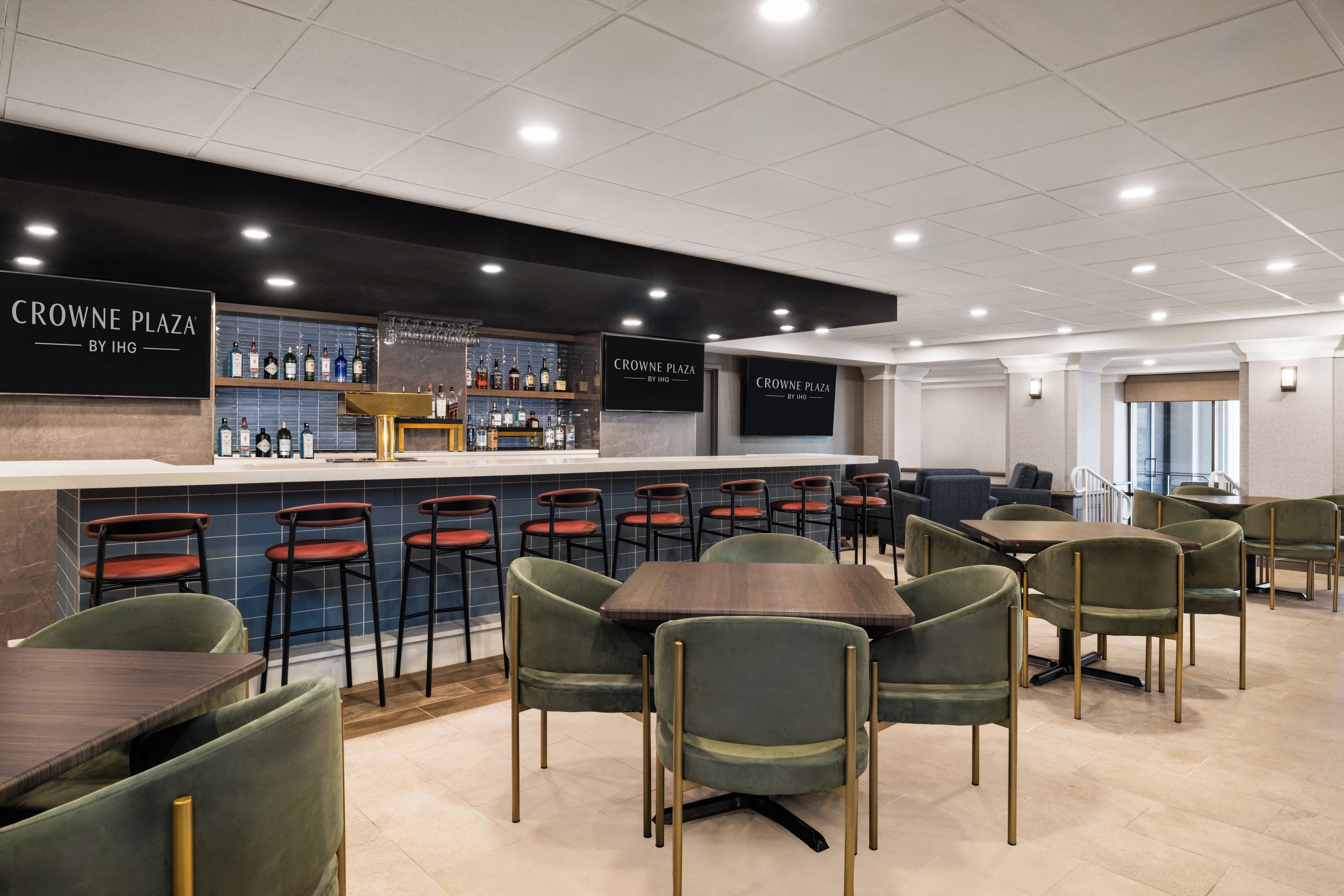 Zona de bar con un letrero que dice 'CROWNE PLAZA BY IHG' y un área de estar con mesas y sillas.