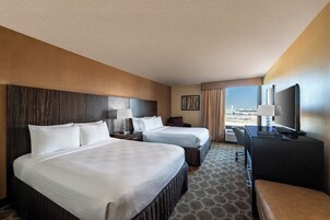 Habitación de hotel con dos camas, un escritorio, un televisor y una ventana con vista a la ciudad.