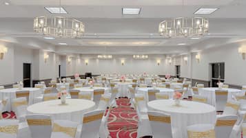 A conference room with round tables, white chairs with gold sashes, and chandeliers.