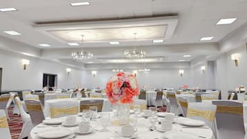 Una sala da banchetto con tavoli rotondi apparecchiati per la cena, ognuno con tovaglie bianche, nastri dorati e composizioni floreali al centro.