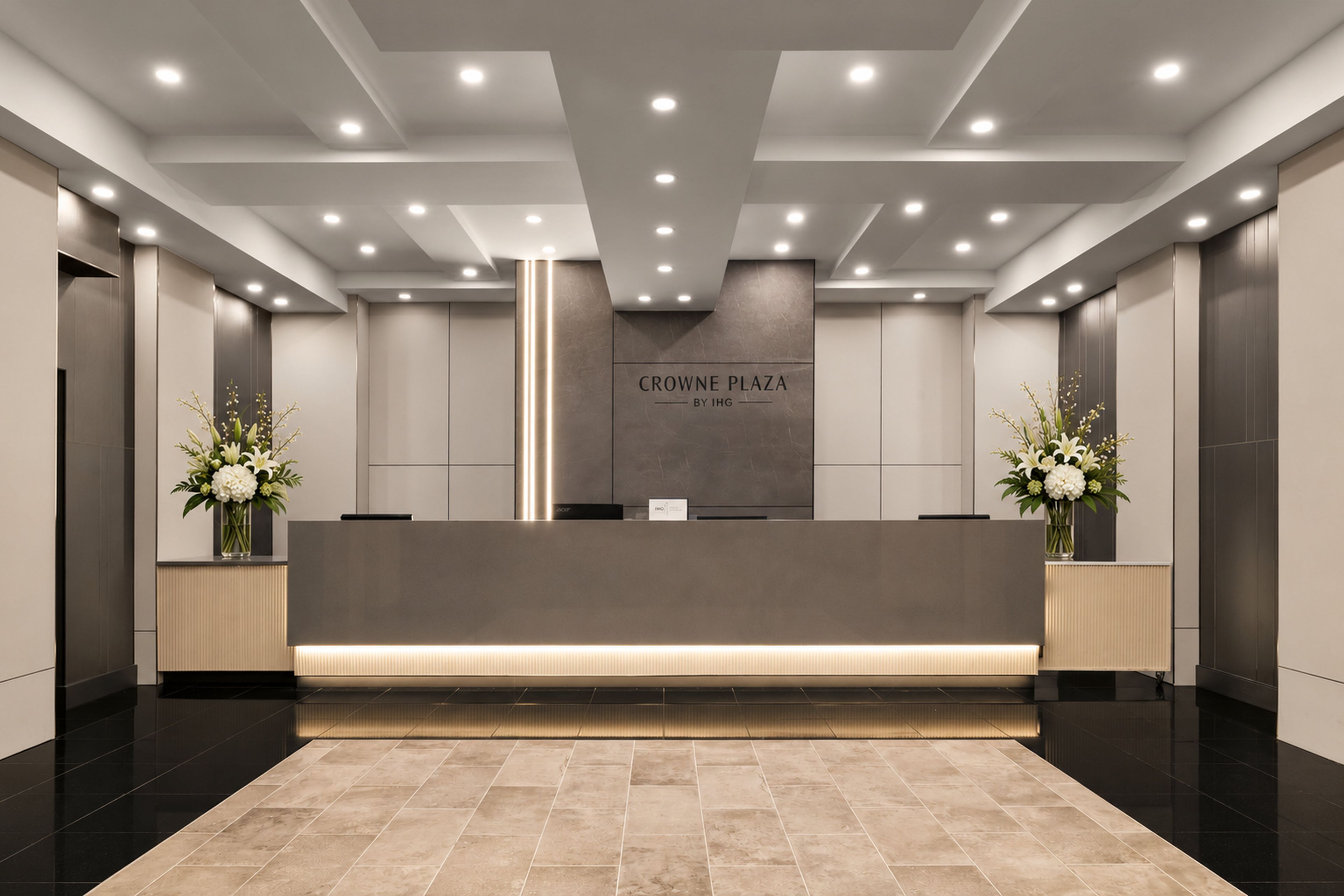 A reception area with a modern design, featuring a reception desk, a vertical light feature, and a sign that reads 'CROWNE PLAZA BY IHG'.