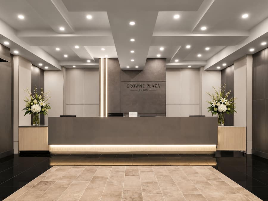 Un área de recepción de diseño moderno, con un mostrador de recepción, un elemento decorativo de iluminación vertical y un cartel que dice 'CROWNE PLAZA BY IHG'.
