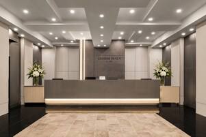 Un área de recepción de diseño moderno, con un mostrador de recepción, un elemento decorativo de iluminación vertical y un cartel que dice 'CROWNE PLAZA BY IHG'.