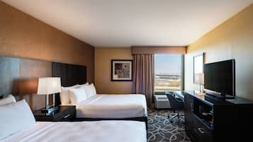 A hotel room with two beds, a desk, a television, and a window with a view.