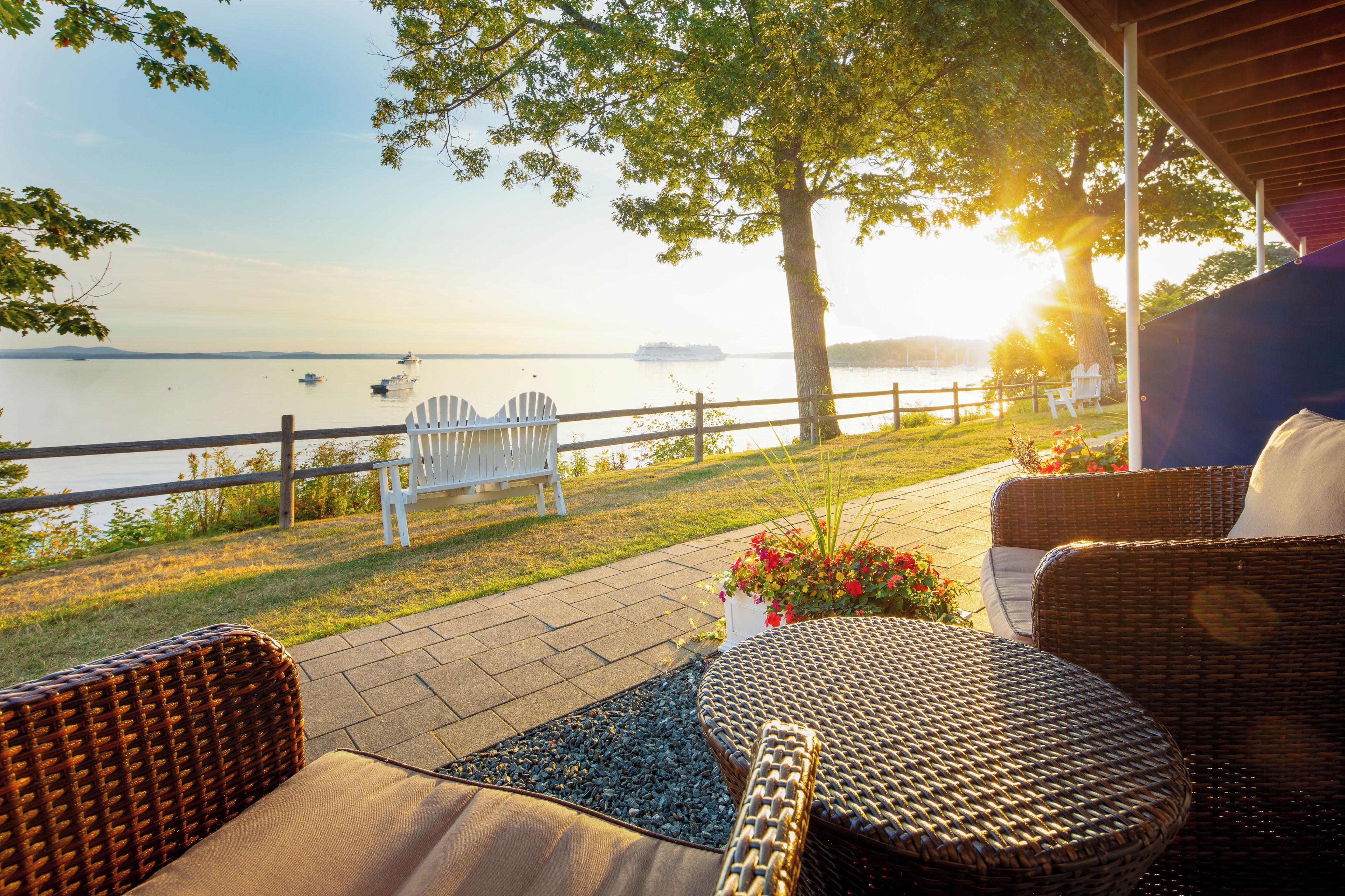 Een terras met rieten meubilair, uitzicht op een rustig meer en een houten hek.