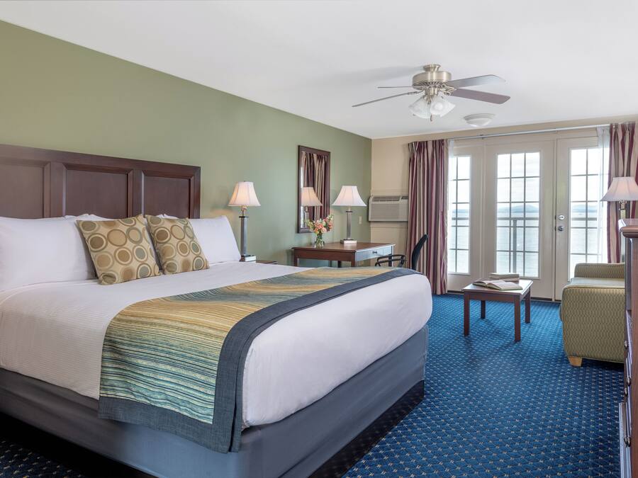 A hotel room with a large bed, two bedside tables with lamps, a desk, a chair, and a view of the outdoors through the door.