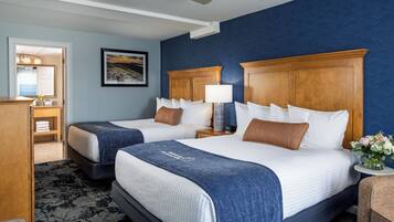 A hotel room with two beds, a wooden headboard, a nightstand with a lamp, a framed picture on the wall, and a bathroom visible through an open door.