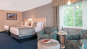 A hotel room with two beds, a round dining table, and a view of trees through the window.