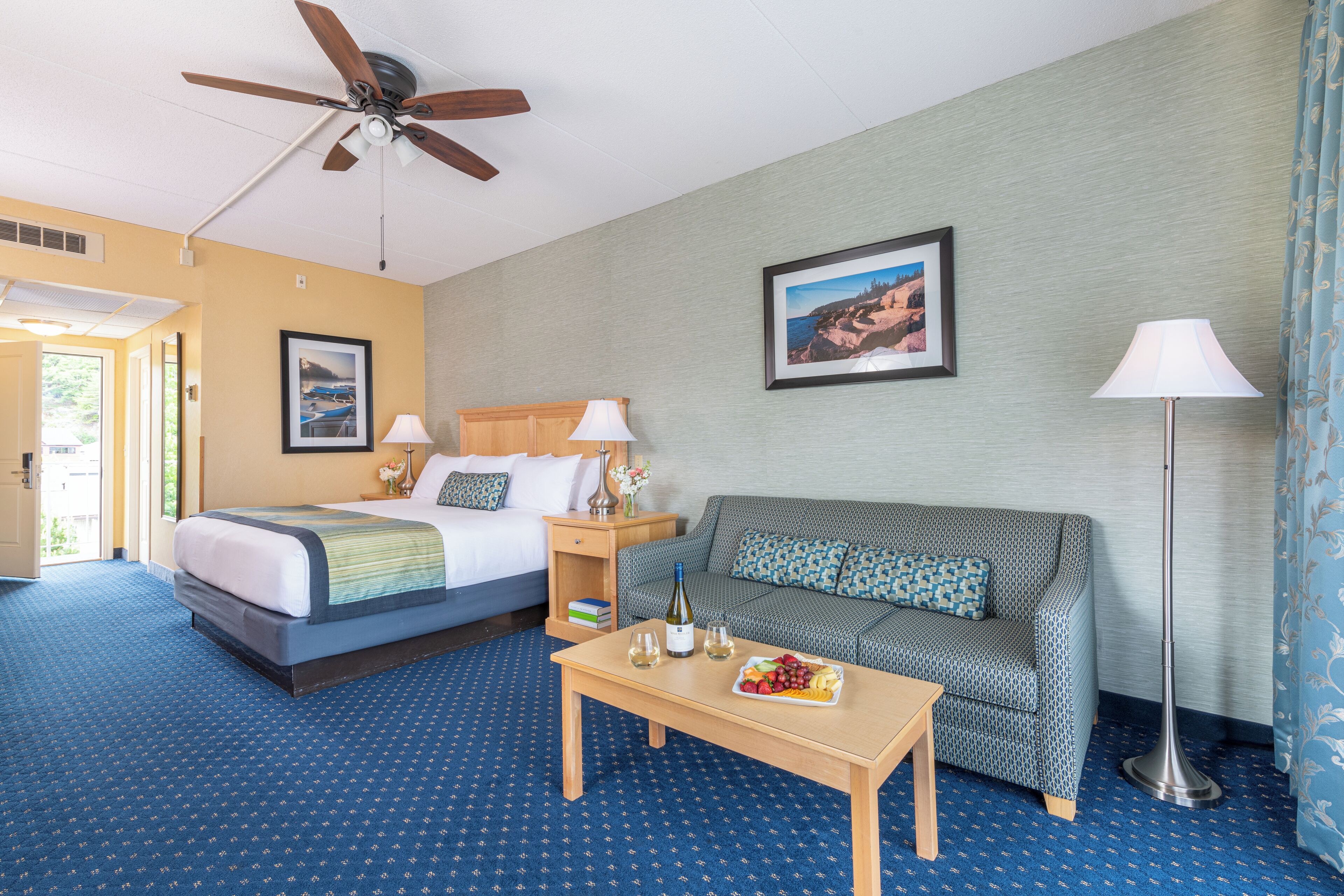 A hotel room with a bed, a sofa, a coffee table, and a ceiling fan.