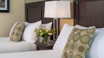 A hotel room with two beds, a nightstand with a lamp, and a vase with flowers.