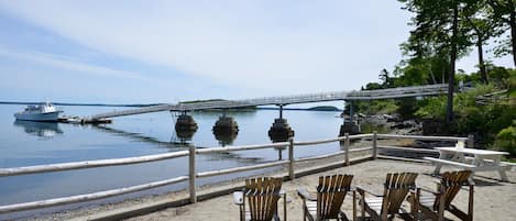 A waterfront area with a wooden deck, chairs, and a bridge over the water.