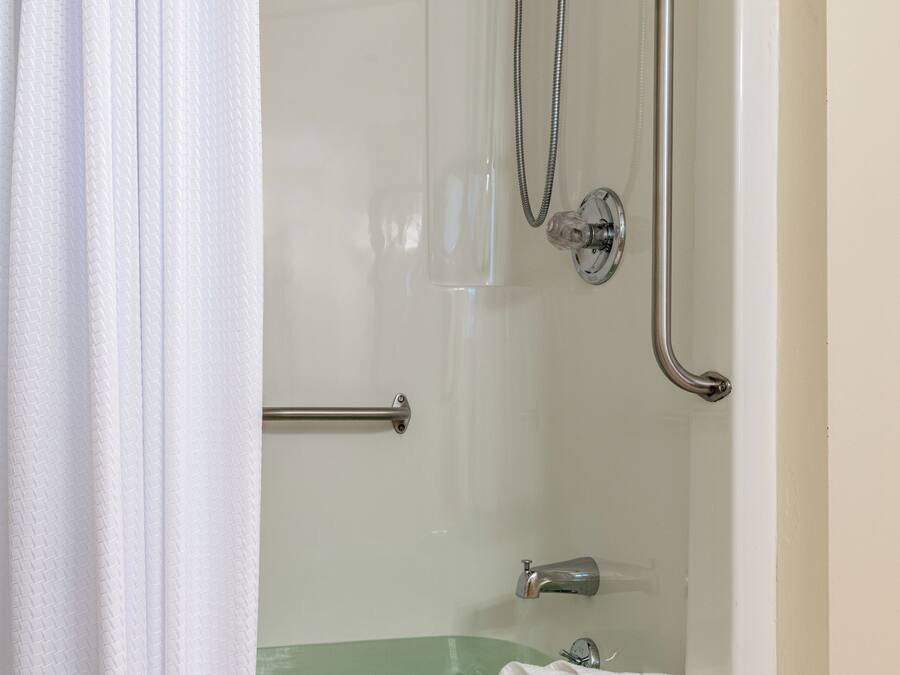 A shower area with a glass door, a handheld showerhead, a grab bar, and a towel on the floor.