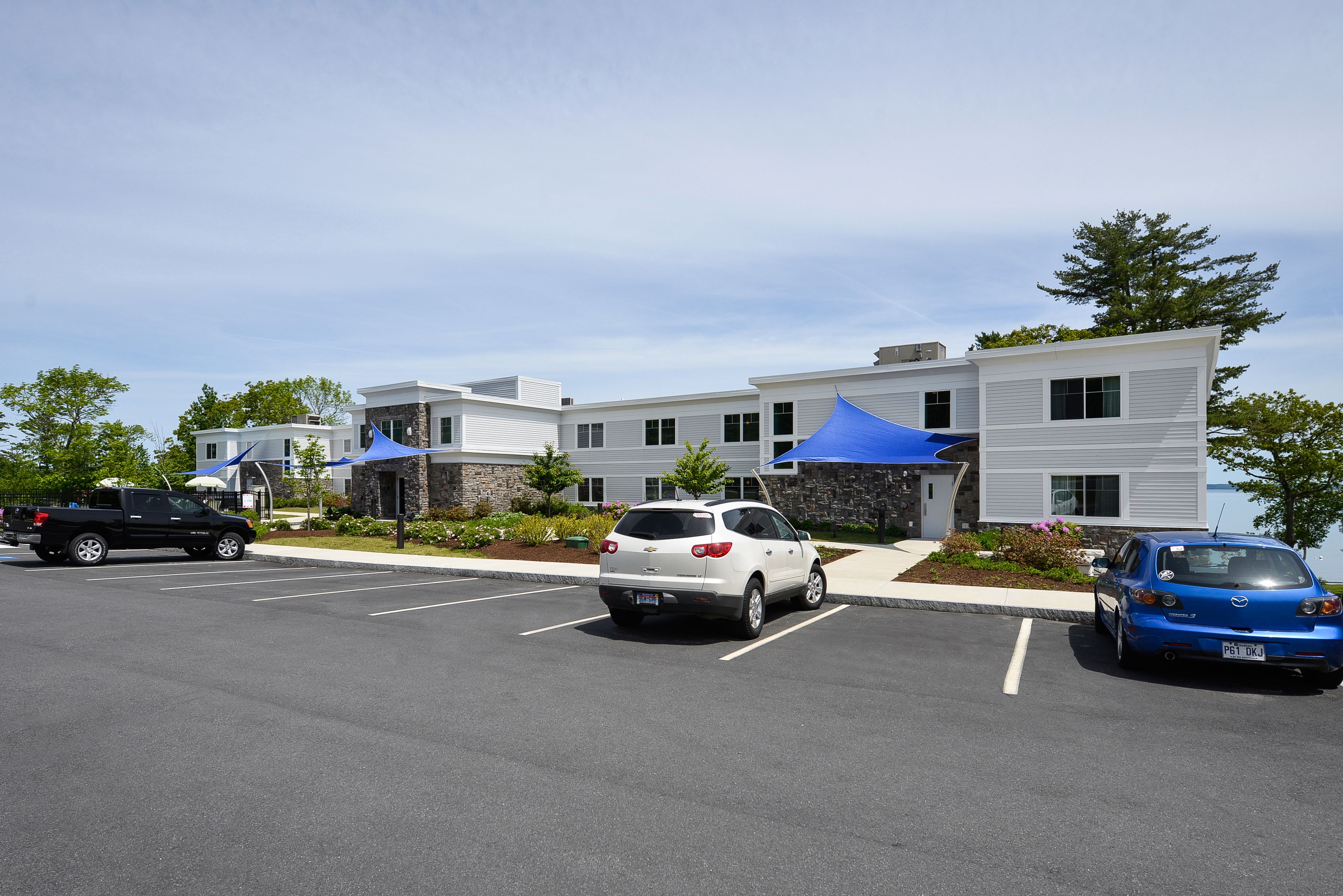 A parking lot with several cars, a building with a modern design, and a landscaped area with plants.