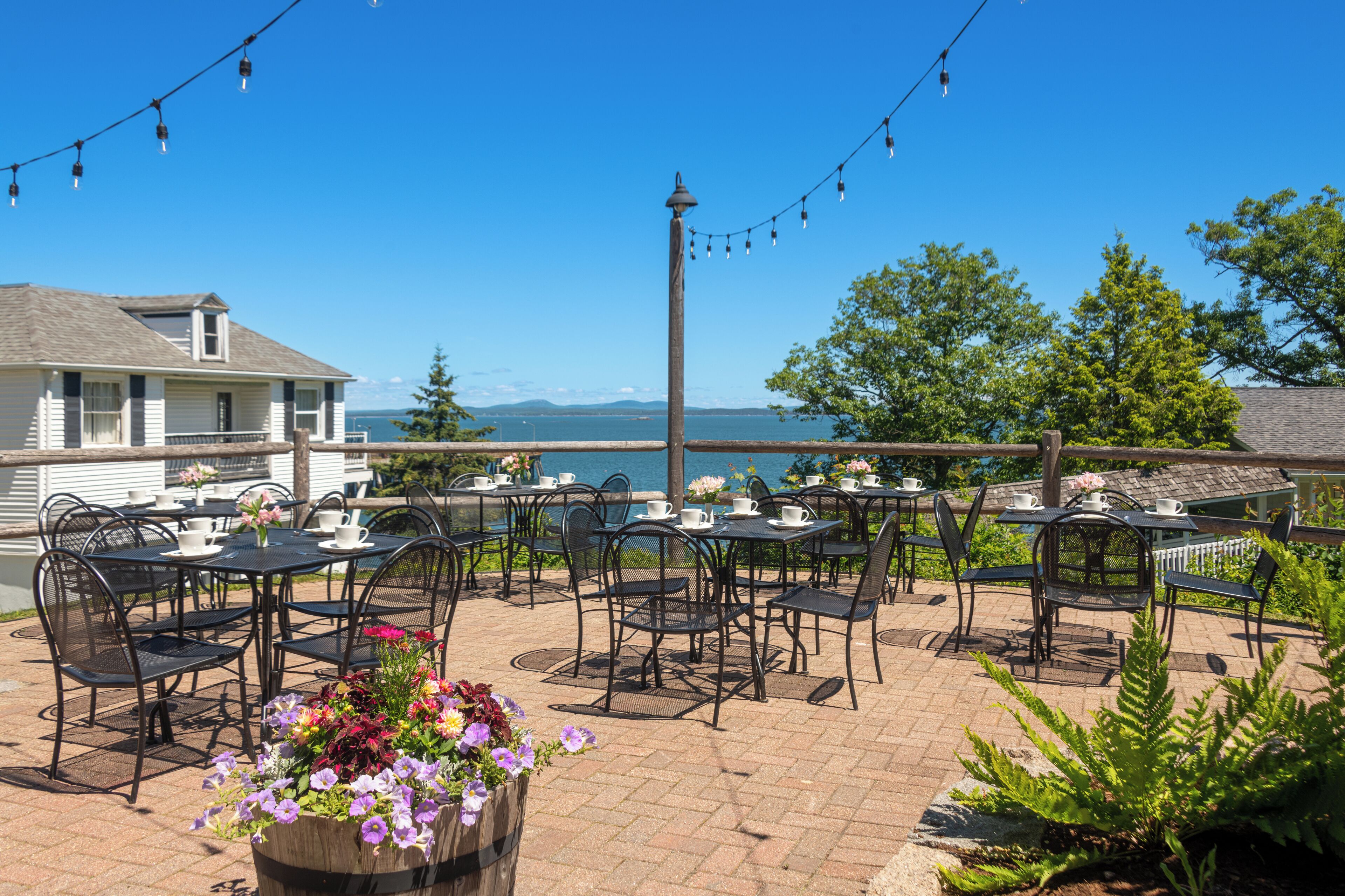 An outdoor patio with tables and chairs, overlooking a body of water and mountains.