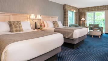 A hotel room with two beds, a ceiling fan, a small table with a lamp, and a view of the outdoors.