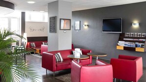 A modern lobby with red seating, a flat-screen TV, and a magazine rack. - Mercure Saint Lo Centre (Saint-Lo)