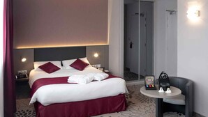 A hotel room with a bed, a round table with a chair, and a door leading to a bathroom. - Mercure Saint Lo Centre (Saint-Lo)