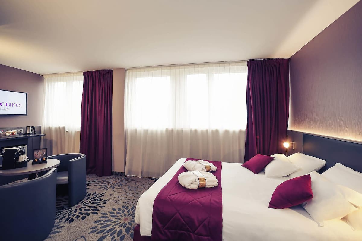 A hotel room with a bed, a desk, a chair, a TV, and a window with curtains.