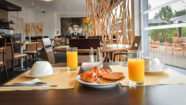 A breakfast setting with croissants, pancakes, and orange juice on a table. - Mercure Saint Lo Centre (Saint-Lo)